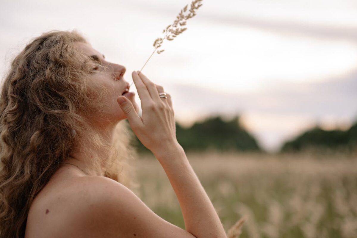 A serene woman with long hair holding grass in her mouth, embracing nature in an open field.